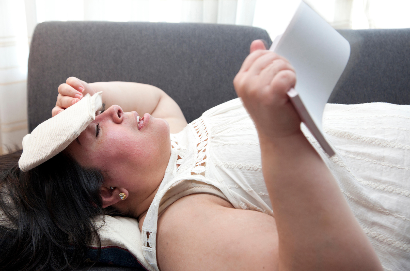 Woman lying on couch with compress on head, fanning herself