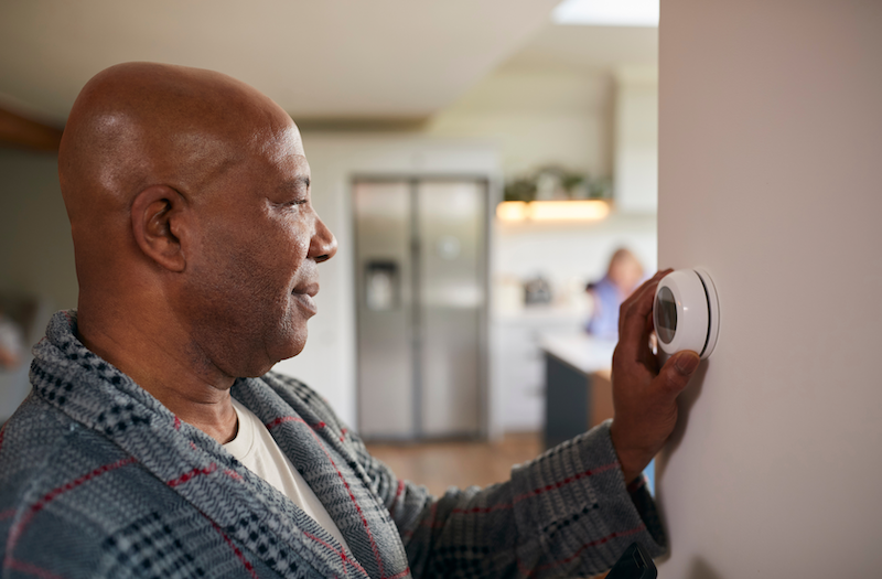 Man in bathrobe adjusting thermostat dial on wall